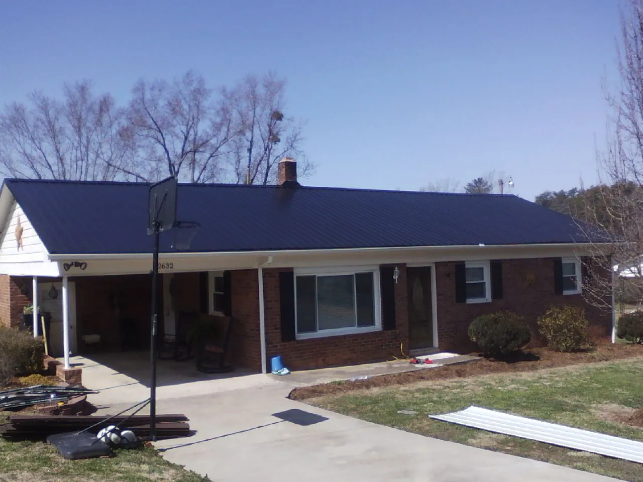 Finished dark blue metal roof on a brick ranch with a carport in Wiggins