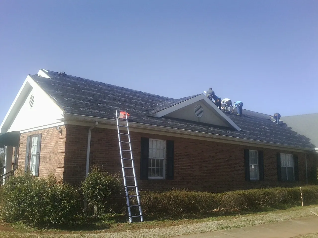 Crew tearing shingles off a brick ranch roof with a ladder set — Metal Roof Repair work by our crew in Wiggins