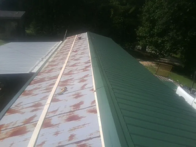Old rusted panels beside newly installed green metal roofing — Wind Damage Roof Repair by Roofing Brothers in Wiggins