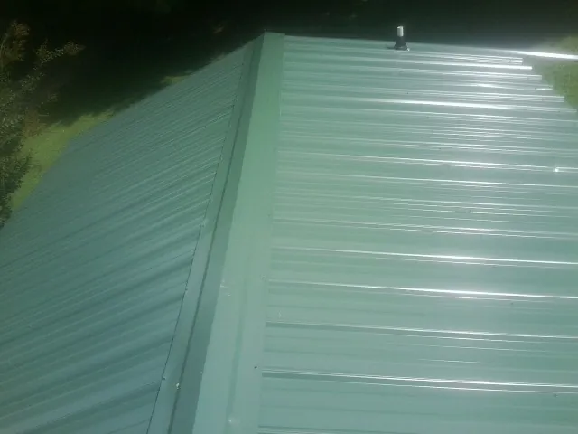 New green metal panels meeting at the ridge of a roof — Flat Roof Repair work by our crew in Wiggins