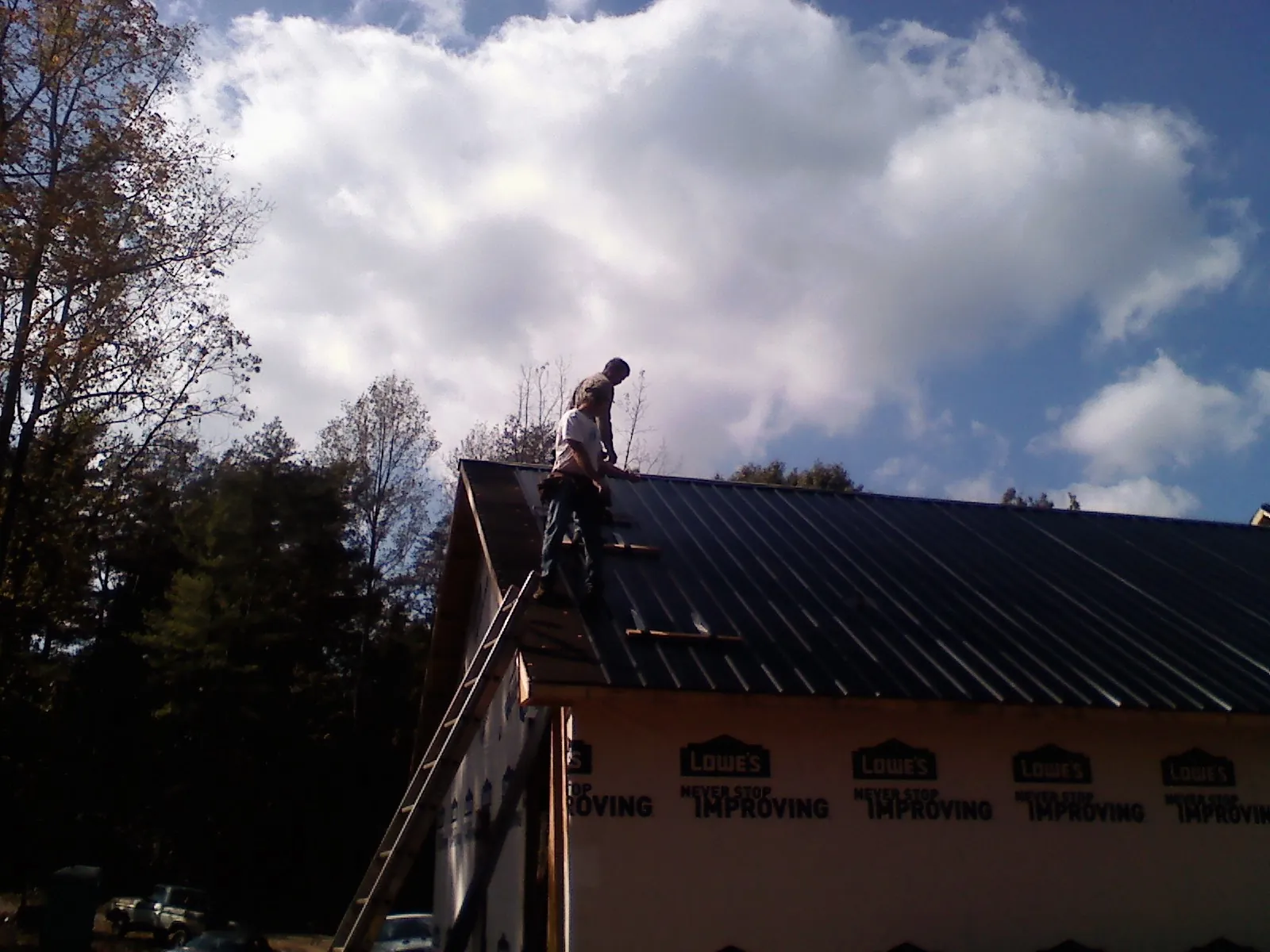 Roofer fastening dark metal panels high against a cloudy sky, from a Roof Inspection job in Wiggins