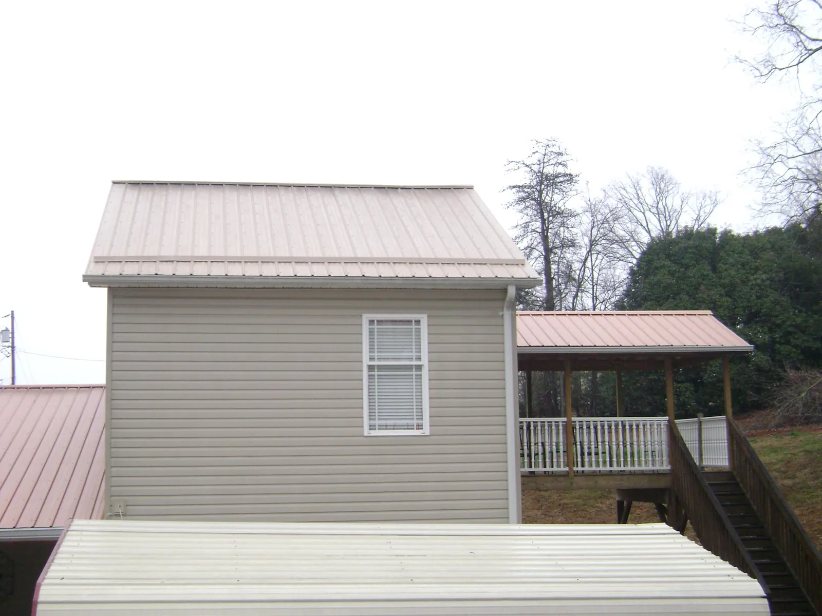 Tan metal roofs on a two story addition and attached porch, from a Roof Replacement job in Wiggins
