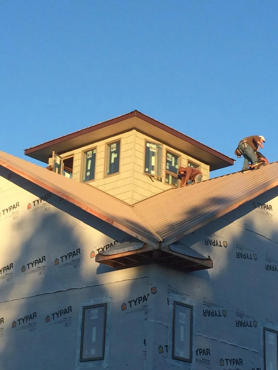 Roofers working around a rooftop cupola on a new metal roof at sunset — Roof Waterproofing in Wiggins by Roofing Brothers
